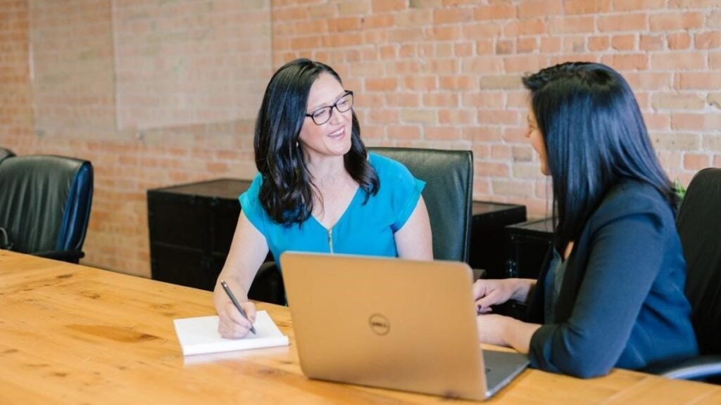 Two women discussing AI orchestration challenges at a table with a laptop open between them